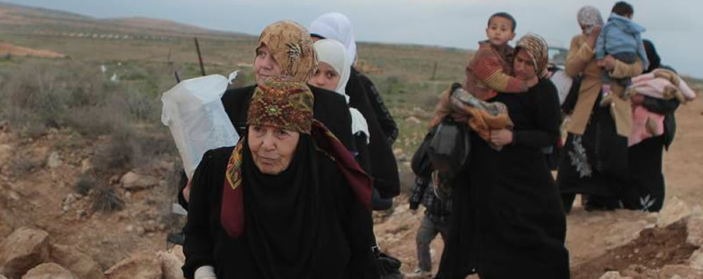 Women dressed in black carrying children along a dusty road